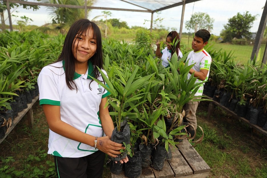 Estudante fardada segurando uma muda de açai